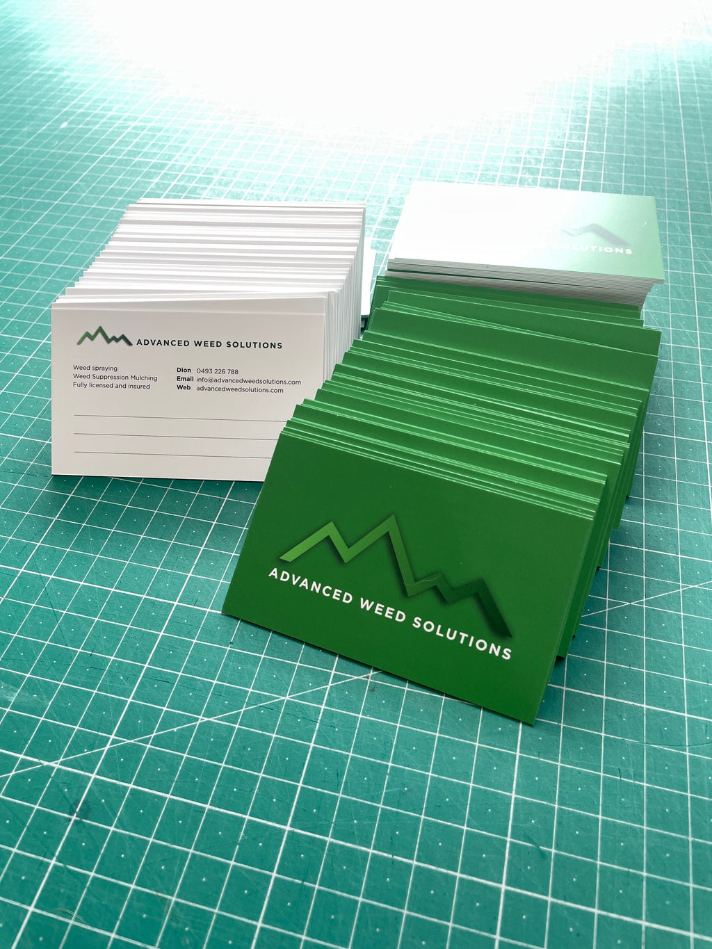 Stack of green business cards with 'Advanced Weed Solutions' on a green grid background