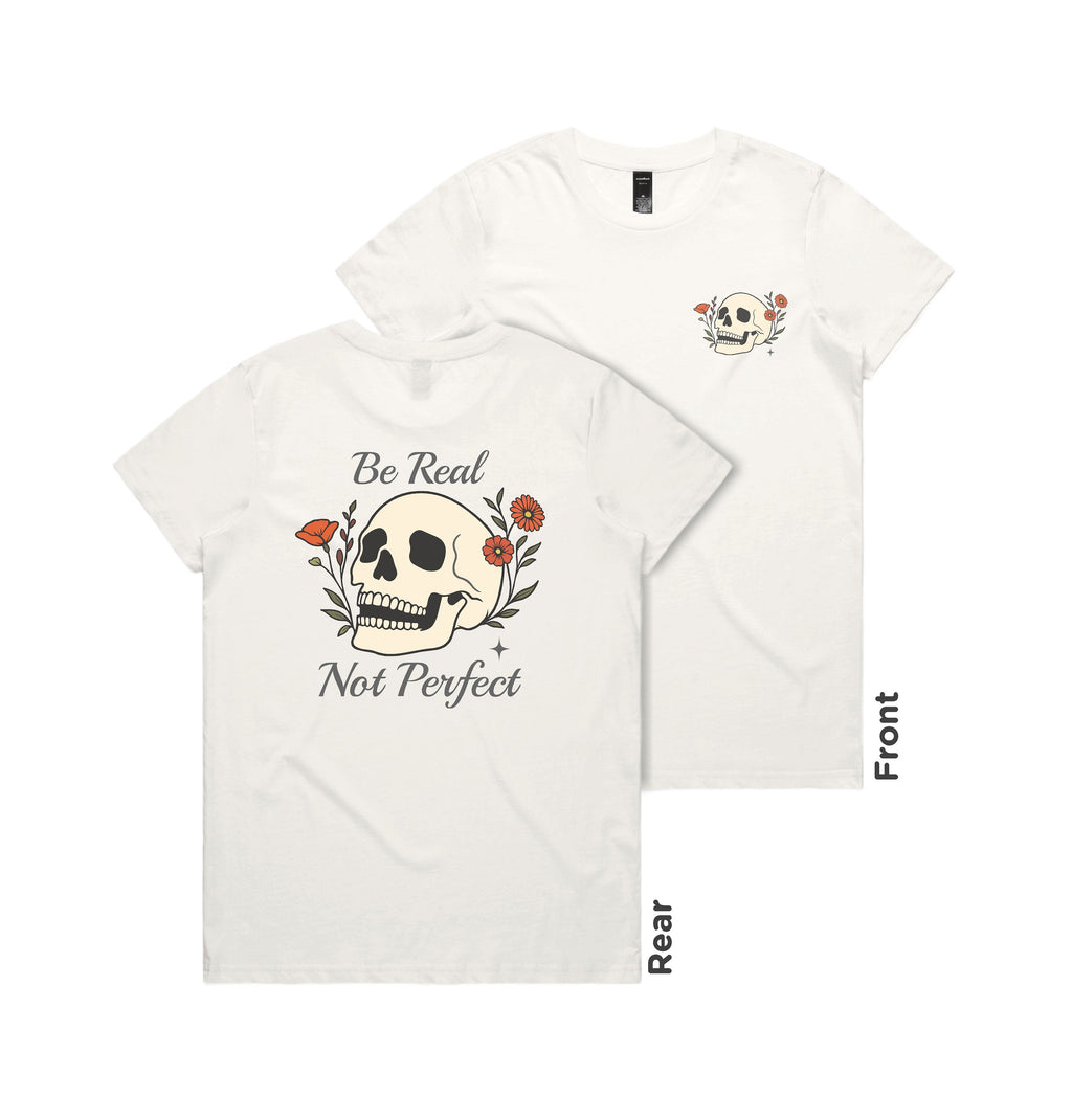 White t-shirt with skull and floral design, 'Be Real Not Perfect' text on a white background